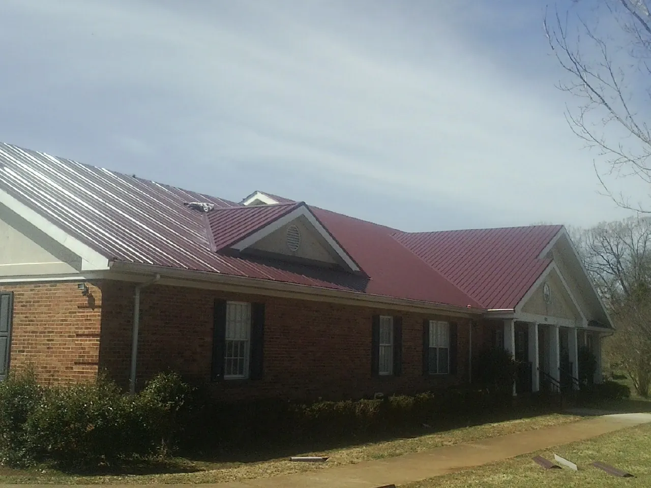 Red metal roof with gabled entries on a long brick building, from a Hail Damage Roof Repair job in Rices Landing