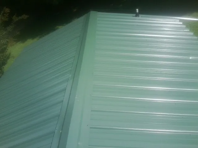 New green metal panels meeting at the ridge of a roof — Flat Roof Repair work by our crew in Rices Landing
