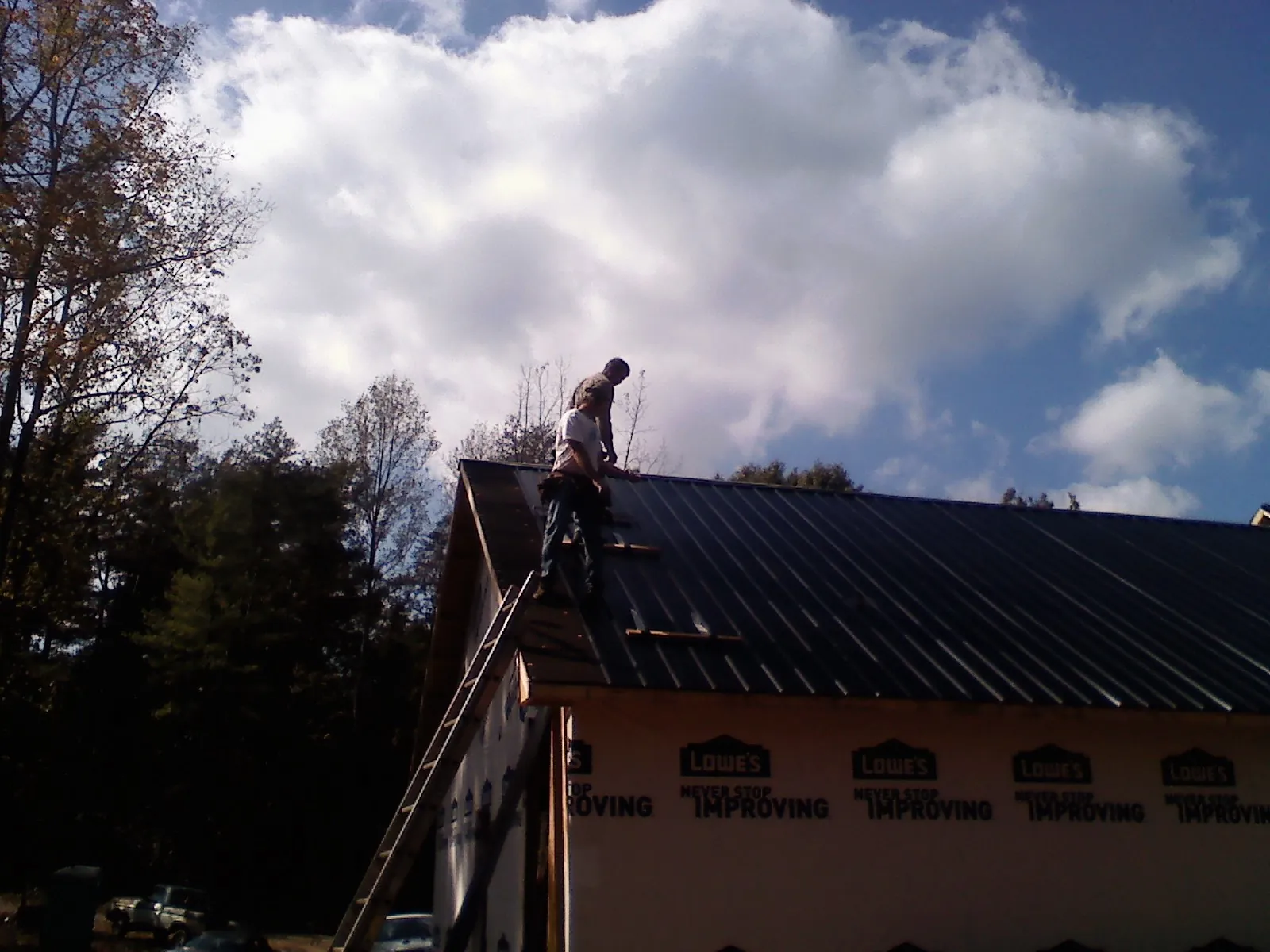 Roofer fastening dark metal panels high against a cloudy sky, from a Roof Inspection job in Rices Landing
