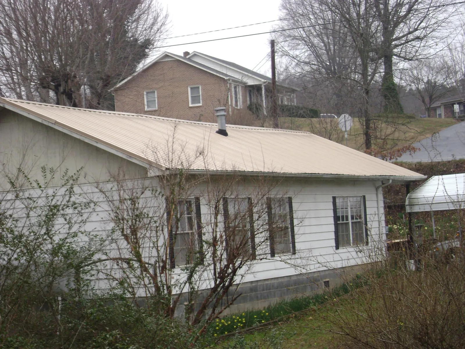 Tan metal roof on a white sided house set into a hillside — Commercial Roofing by Roofing Brothers in Rices Landing